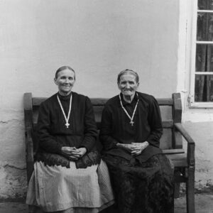 Dwie kobiety w sędziwym wieku ubrane tradycyjnie w śląskie stroje ludowe – jakle (kaftany) i mazelonki (spódnice ze stanikiem). Po lewej: Maria Porada. Oleszka (niem. Oleschka), koniec lat 30. XX w.