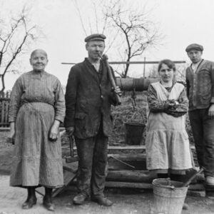Praca w obejściu – rodzice wraz z dorastającymi dziećmi w ubraniach roboczych. W tle przydomowa studnia z drewnianym kołowrotem. Oleszka (niem. Oleschka), lata 30. XX w.