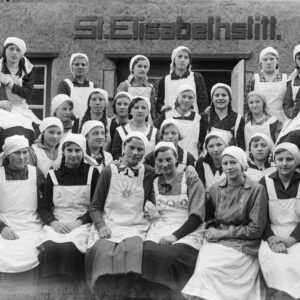 Młode kobiety przed budynkiem Fundacji św. Elżbiety (niem. St. Elisabethstiftung) w Żyrowej, w którym działało przedszkole i w którym organizowano kursy gotowania oraz kroju i szycia dla miejscowych dziewcząt. Na zdjęciu m.in. Jadwiga Knop (druga z prawej w dolnym rzędzie) oraz Gertruda Smiatek (trzecia z prawej w górnym rzędzie). Żyrowa (niem. Zyrowa), około 1930 r.